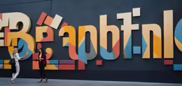two women walk past a huge colorful wall