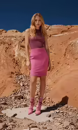 a woman standing on rocks in a pink dress