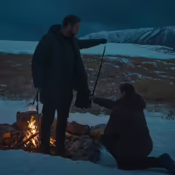 a couple cooking food over a campfire in the snow