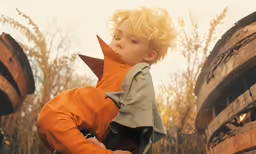 young boy in orange and grey clothes sitting on wooden barrel