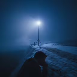 a man in black hoodie sitting under a street light at night