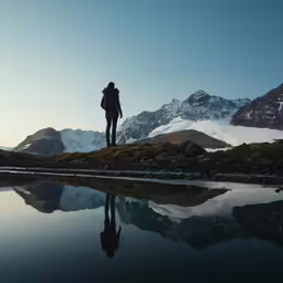 a person standing by the lake looking at mountains