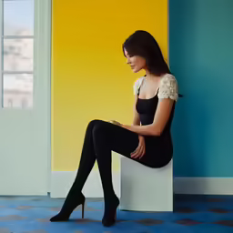 a young woman wearing all black poses in a brightly colored room