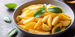 a bowl filled with sliced mangoes and topped with green leaves