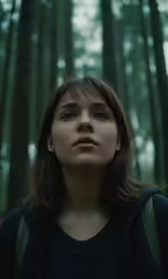 a girl is staring into the camera in front of some tall trees