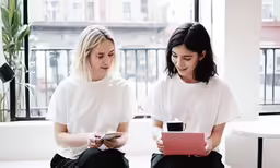 two women sitting side by side in front of a window