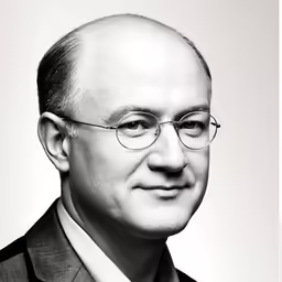 a black and white photo of a bald man in suit and tie