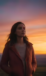a woman in a parka stares into the sunset