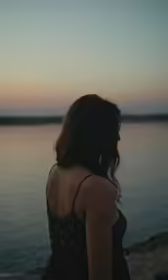 woman with long hair looks out over water at sunset