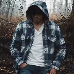 a guy with a hoodie stands in the woods
