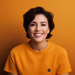 woman in yellow t - shirt smiling at camera with orange background