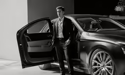 a black and white image of a man standing beside a car