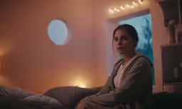 a woman is sitting on her bed in the evening