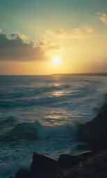 the sun is setting behind the ocean and rocky shore