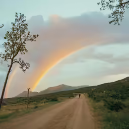 a dirt road going up to a mountain with a rainbow coming out of the clouds