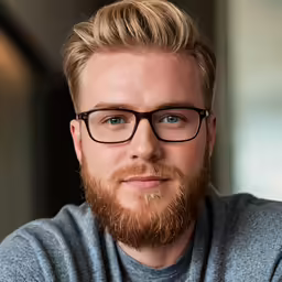 a male with a beard and glasses poses for a portrait