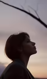 the woman stands at sunset against a blue, cloudy sky