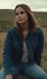 a woman sitting on top of a log in a grassy field