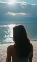 a young woman looks out over the water as she sits on a beach