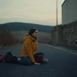there is a woman sitting on the street near a suitcase