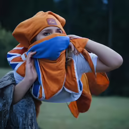 the girl wearing an orange hat is covering her eyes with a blue scarf