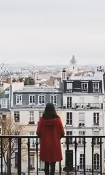 a girl in red coat looking out the balcony