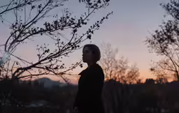 a woman in black standing next to a tree