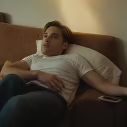 a man sleeping on a brown couch next to a remote control