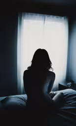 a woman sitting on a bed in a dark room
