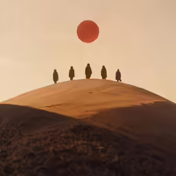 four people stand on a hill with a full red ball overhead