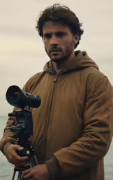 a man in a brown jacket is holding a camera