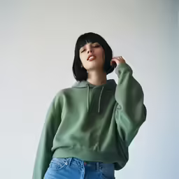 the young woman wears a green sweater, jeans, and white shoes