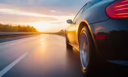 the rear end of a black sports car driving down a road