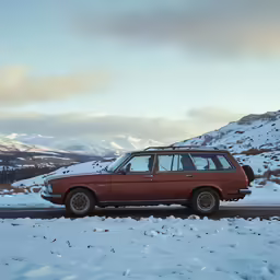an old red station wagon drives in a snowy mountain range