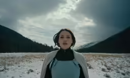 the young woman is looking back with a mountain in the background