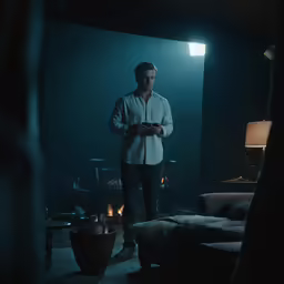 a man standing in a darkened room holding a cell phone