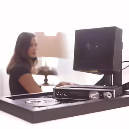 a woman sitting next to a television on top of a table