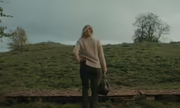 a young woman holding a bag looking back on a hillside