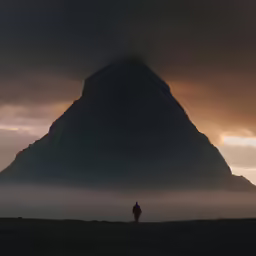 the person stands at the edge of the mountainside in front of a dark tower