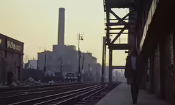 a train track and buildings at dusk, with a person walking along the tracks