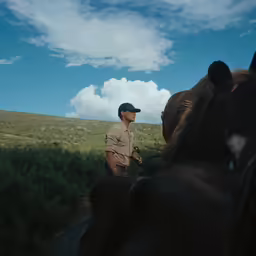 a man standing next to two brown horses on a field