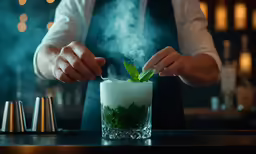 the bartender is holding the shot glass and stirring it with smoke