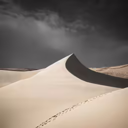 storm clouds loom over a long straight sand dune