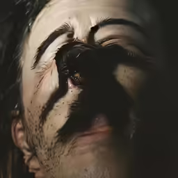 a man with long hair and eyes partially covered by an insect
