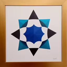a gold frame with black, blue and white shapes,this is an artistic piece of art featuring two squares,a geometric artwork piece mounted in a wood frame,an image of an artistic blue star on white paper,a picture of an art work with paper and glue on it