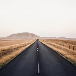 a long empty street between grassy field with mountains