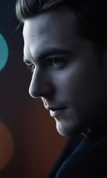 a man with blue eyes stares ahead while standing next to a wall
