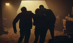 two men are standing in front of light in a darkened room