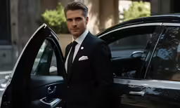 there is a man in a black suit standing beside a car