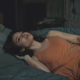 a woman in an orange shirt laying down on a bed